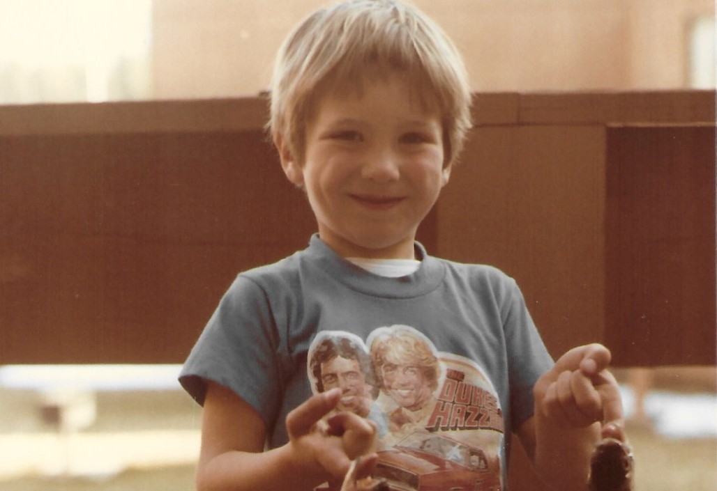Brandon as a young boy smiling in a Dukes of Hazzard t-shirt